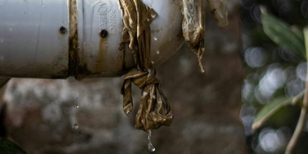 Close-up of a leaking plastic pipe outdoors with water dripping, showing wear and tear.